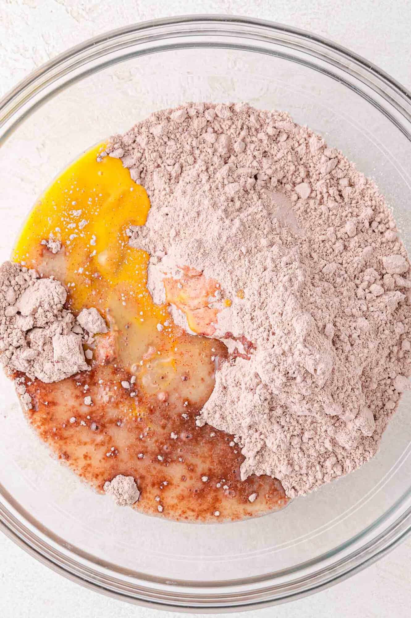 A clear bowl containing raw egg, red velvet cake mix, and other ingredients before mixing.