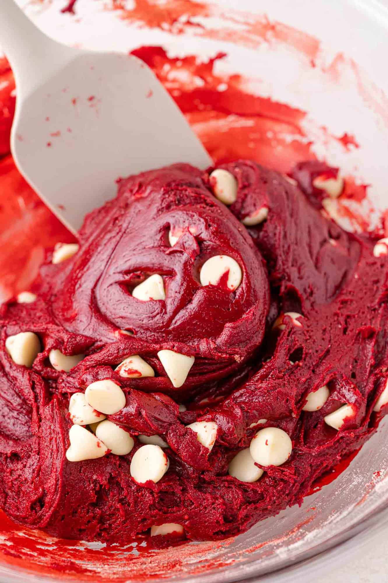 Bowl of red velvet cookie dough with white chocolate chips and a spatula.