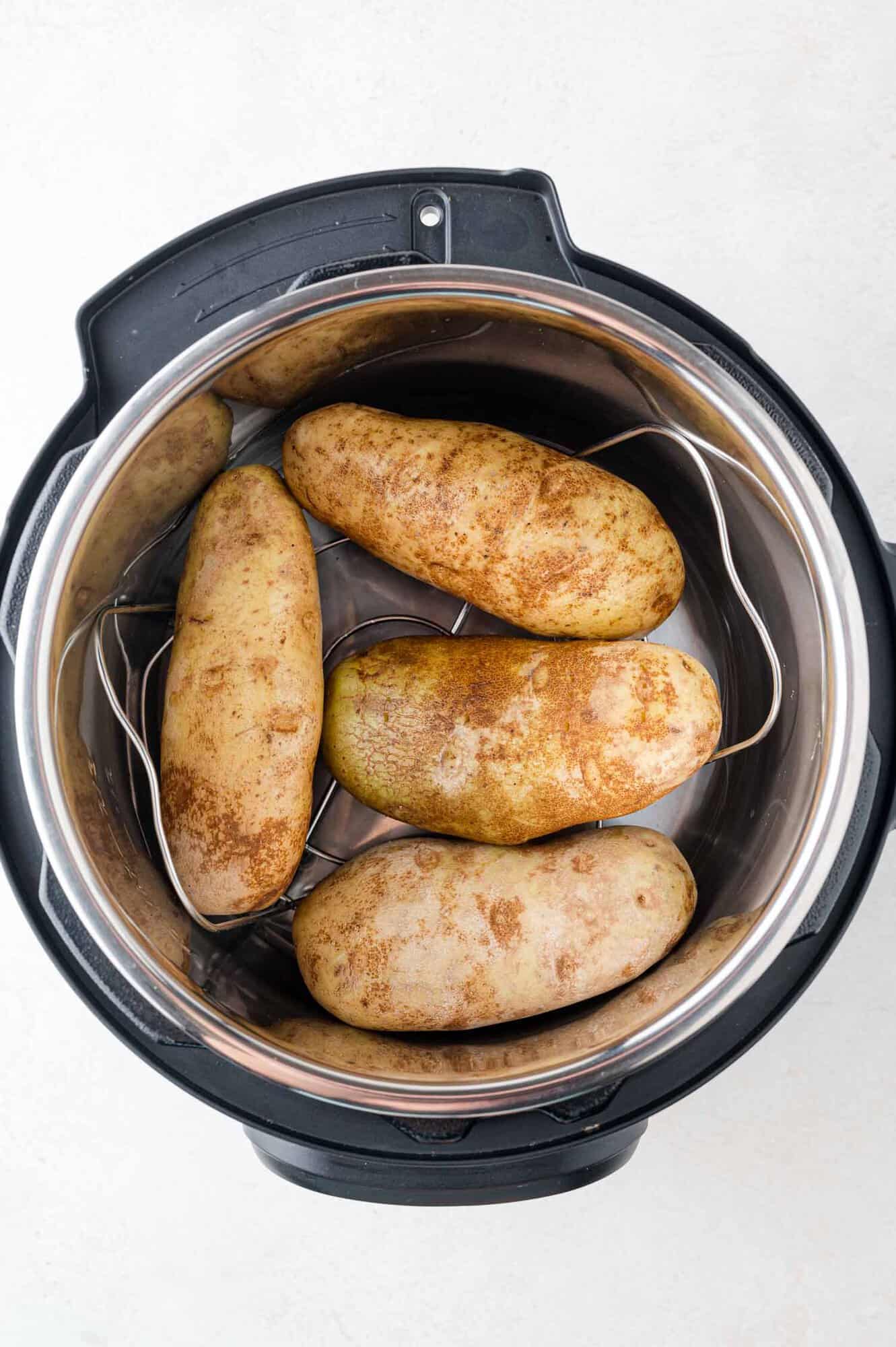 Four raw potatoes in an Instant Pot on a trivet, ready to be cooked.