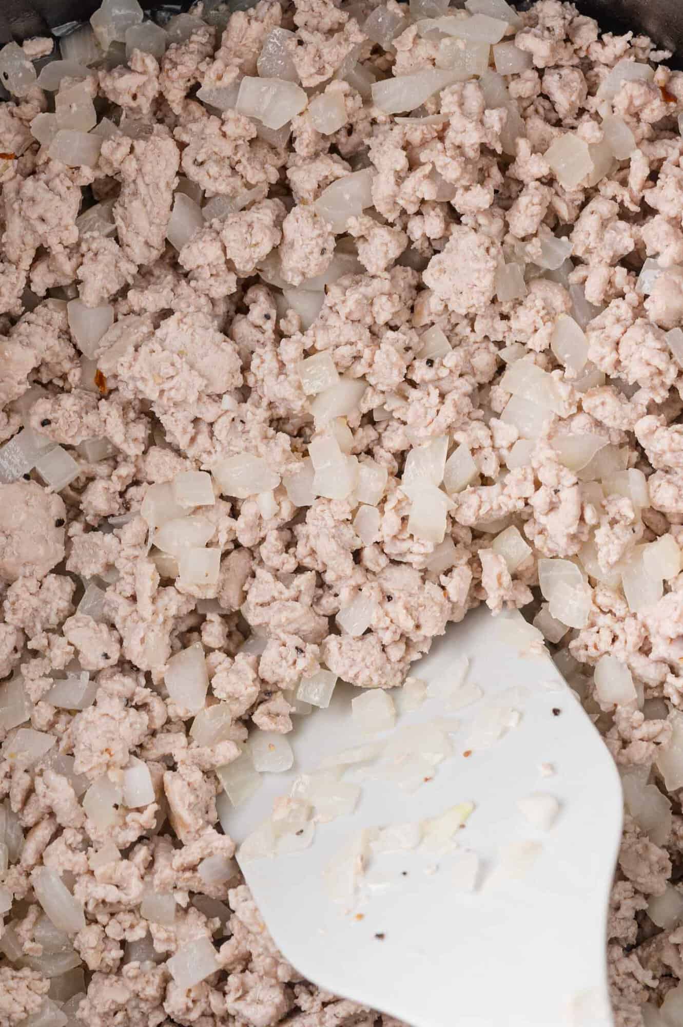 Ground meat and diced onions cooking in a pan with a white spatula.