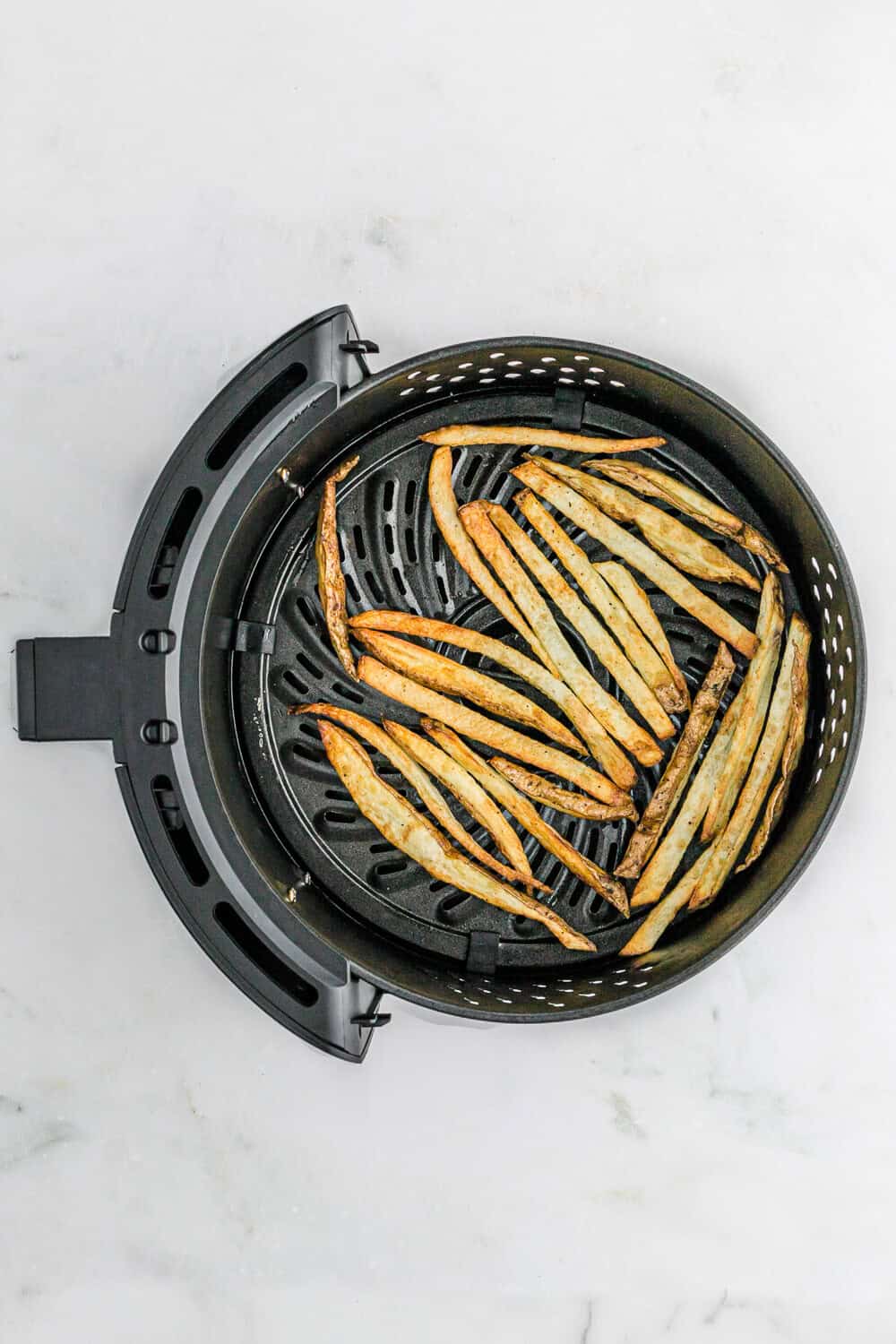 Thin, golden-brown fries in an air fryer basket on a white surface.