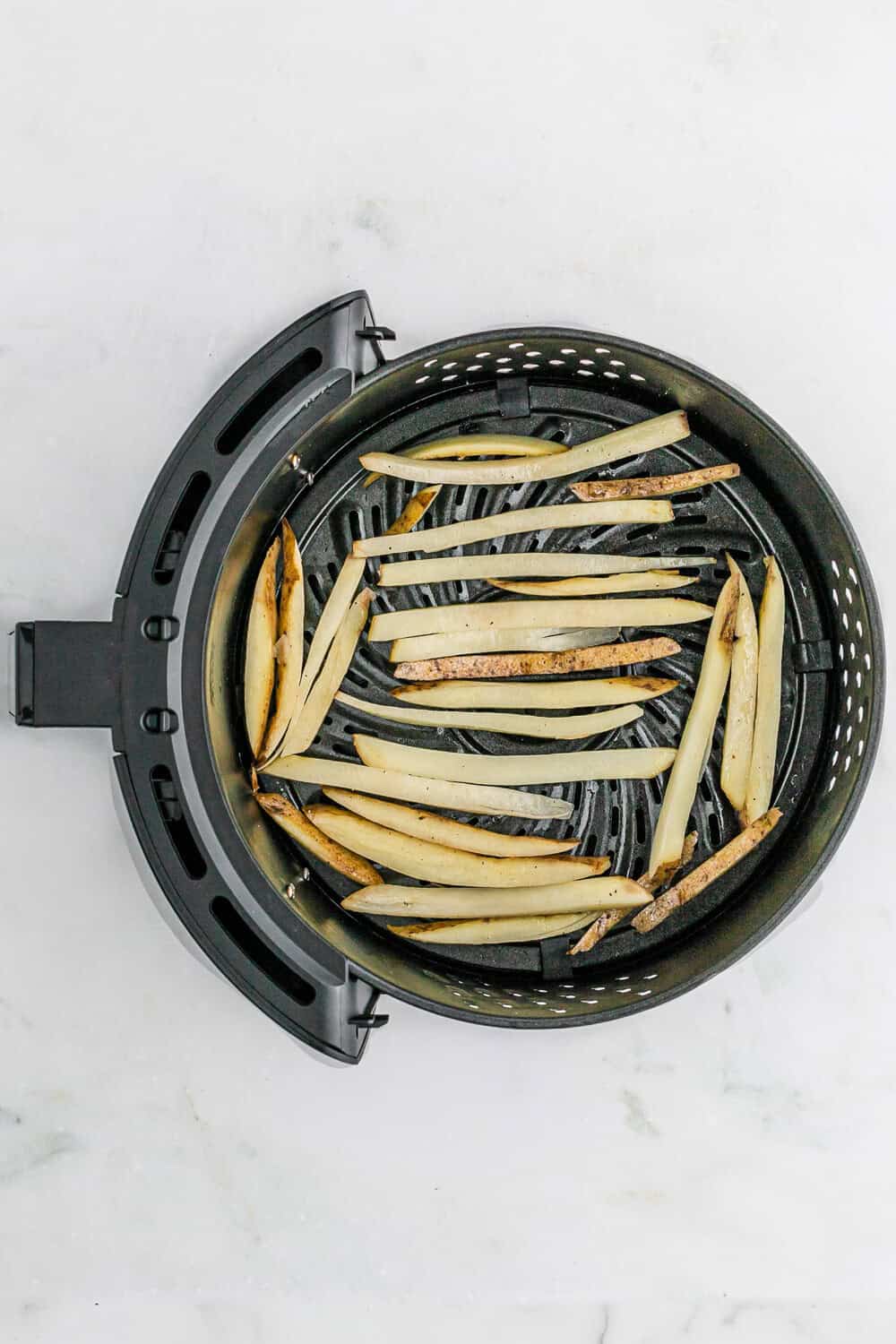 Sliced potatoes arranged in a single layer inside an air fryer basket on a white surface.