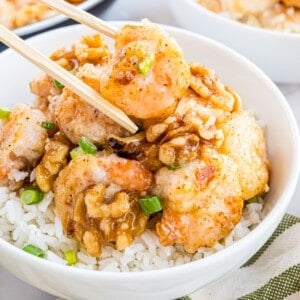 Bowl of rice topped with shrimp, walnuts, and chopped green onions. Chopsticks resting on the side.