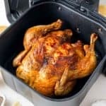 Roasted chicken in an air fryer basket, golden and crispy, with visible seasonings.