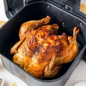Roasted chicken in an air fryer basket, golden and crispy, with visible seasonings.