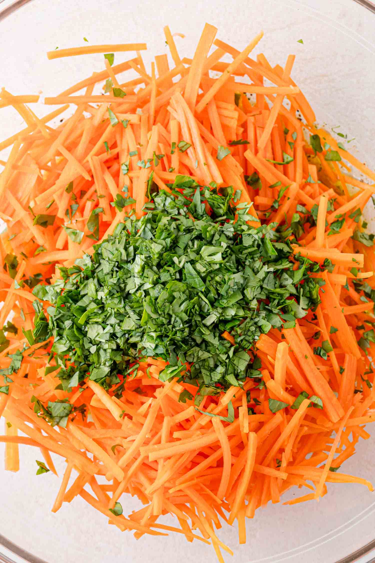 Shredded carrots topped with chopped cilantro in a glass bowl.