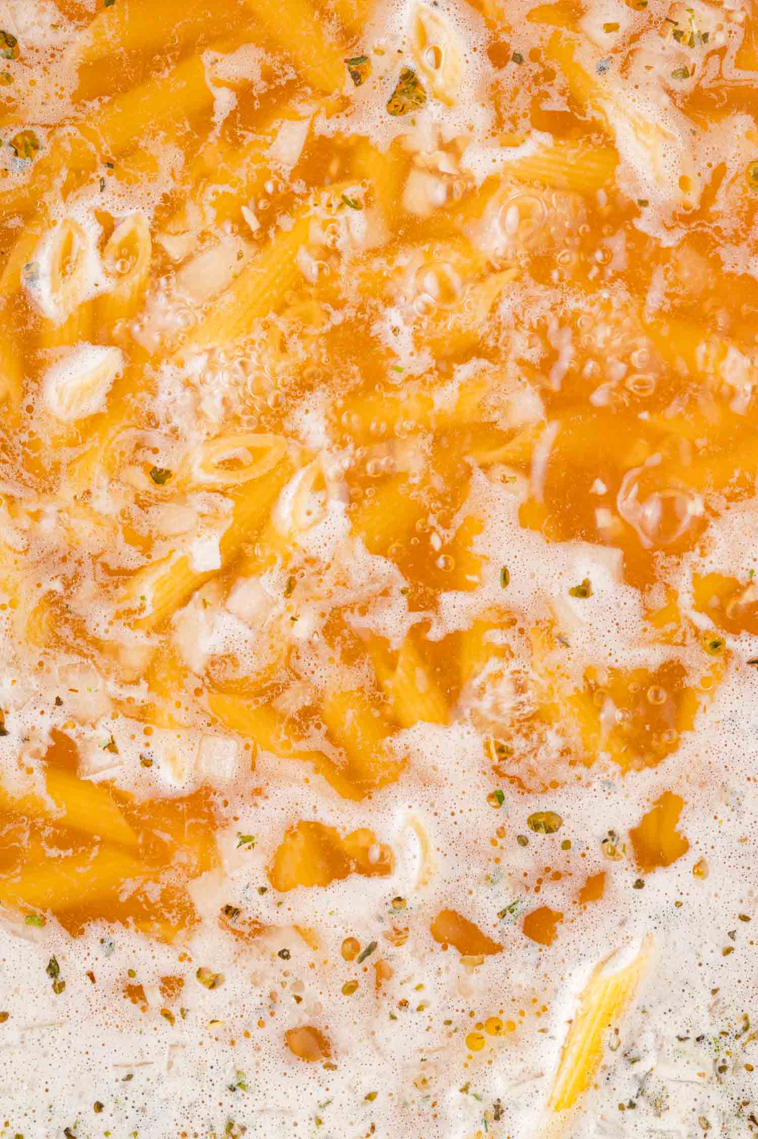 Boiling pasta in broth with visible herbs and bubbling liquid.