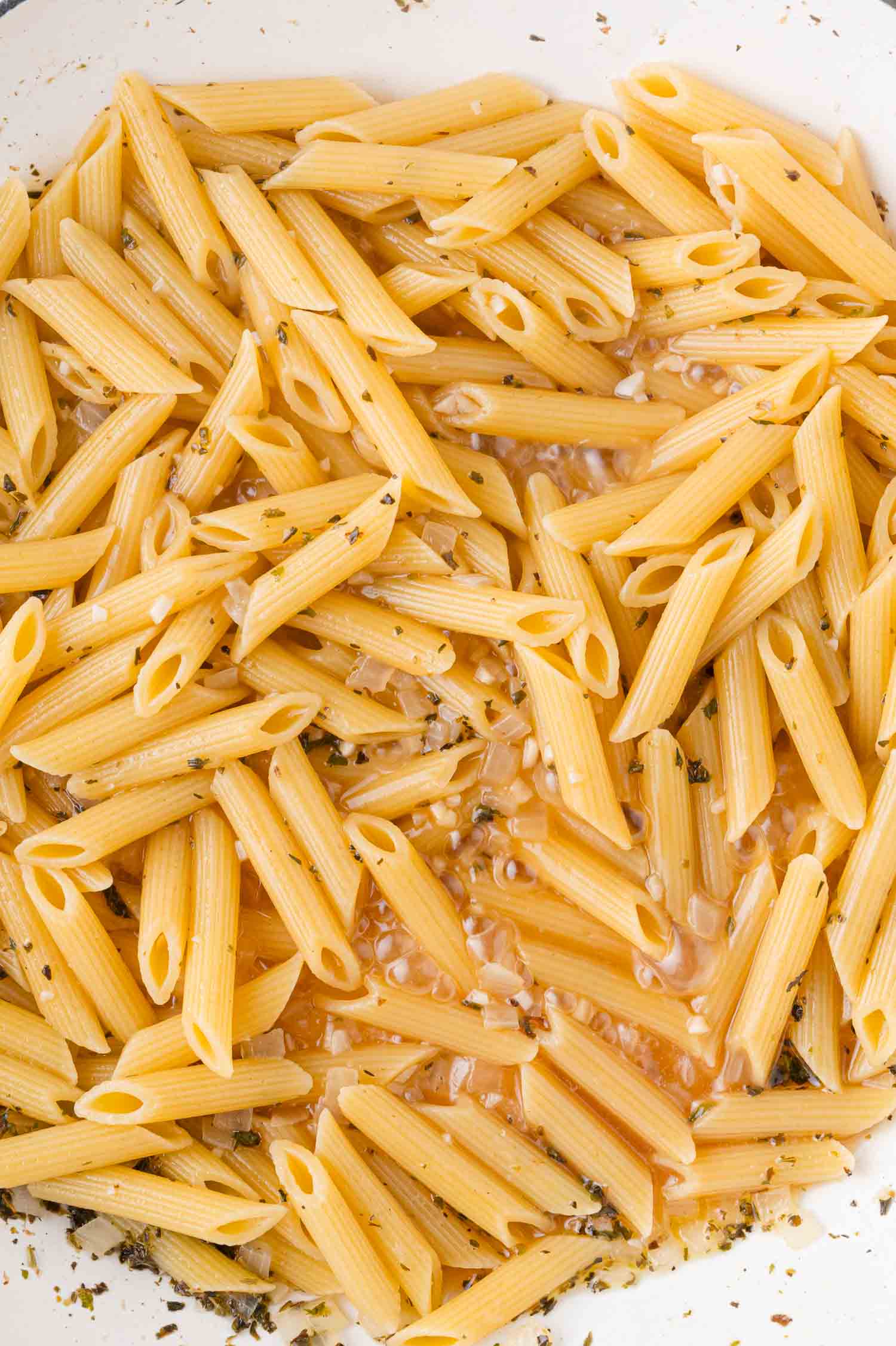 A plate of cooked penne pasta with herbs, sitting in a light sauce.