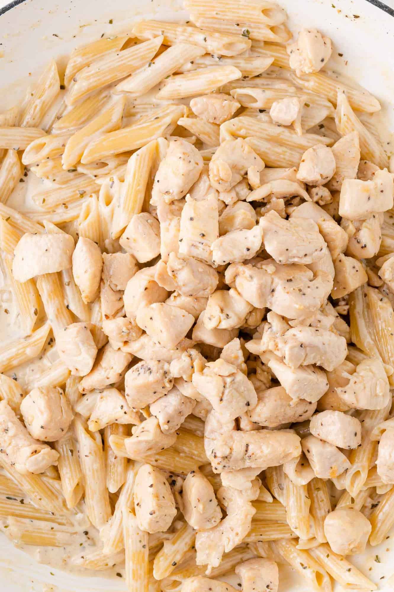Penne pasta with chunks of cooked chicken in a creamy sauce, seasoned with herbs and spices.