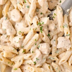 Close-up of creamy pasta with penne, chunks of chicken, and parsley garnish.