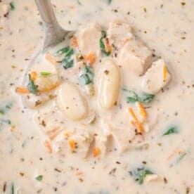 Creamy soup with chunks of chicken, gnocchi, spinach, and diced vegetables, garnished with herbs.