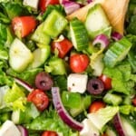 Close-up of a fresh Greek salad with tomatoes, cucumbers, red onions, olives, feta cheese, and lettuce, mixed with a wooden spoon.