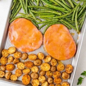 Sheet pan with glazed ham steaks, roasted baby potatoes, and green beans.