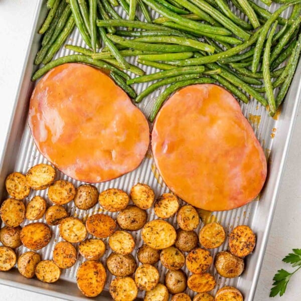 Sheet pan with glazed ham steaks, roasted baby potatoes, and green beans.