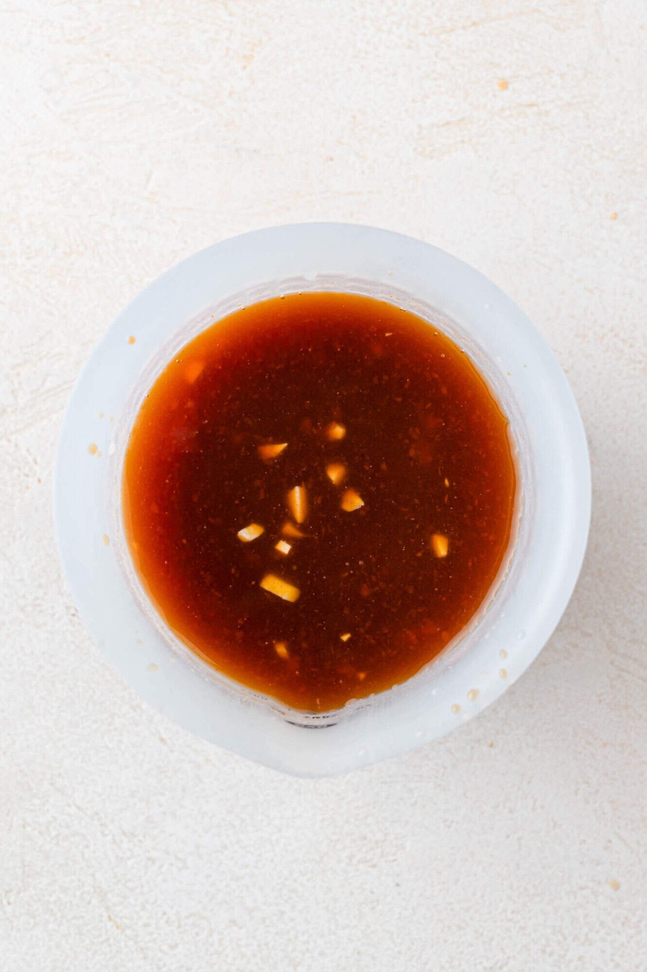 Top view of a bowl containing a brown sauce with visible small chunks, placed on a light textured surface.