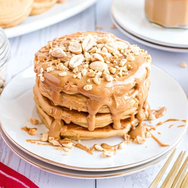 A stack of pancakes topped with peanut butter and chopped peanuts on a white plate.