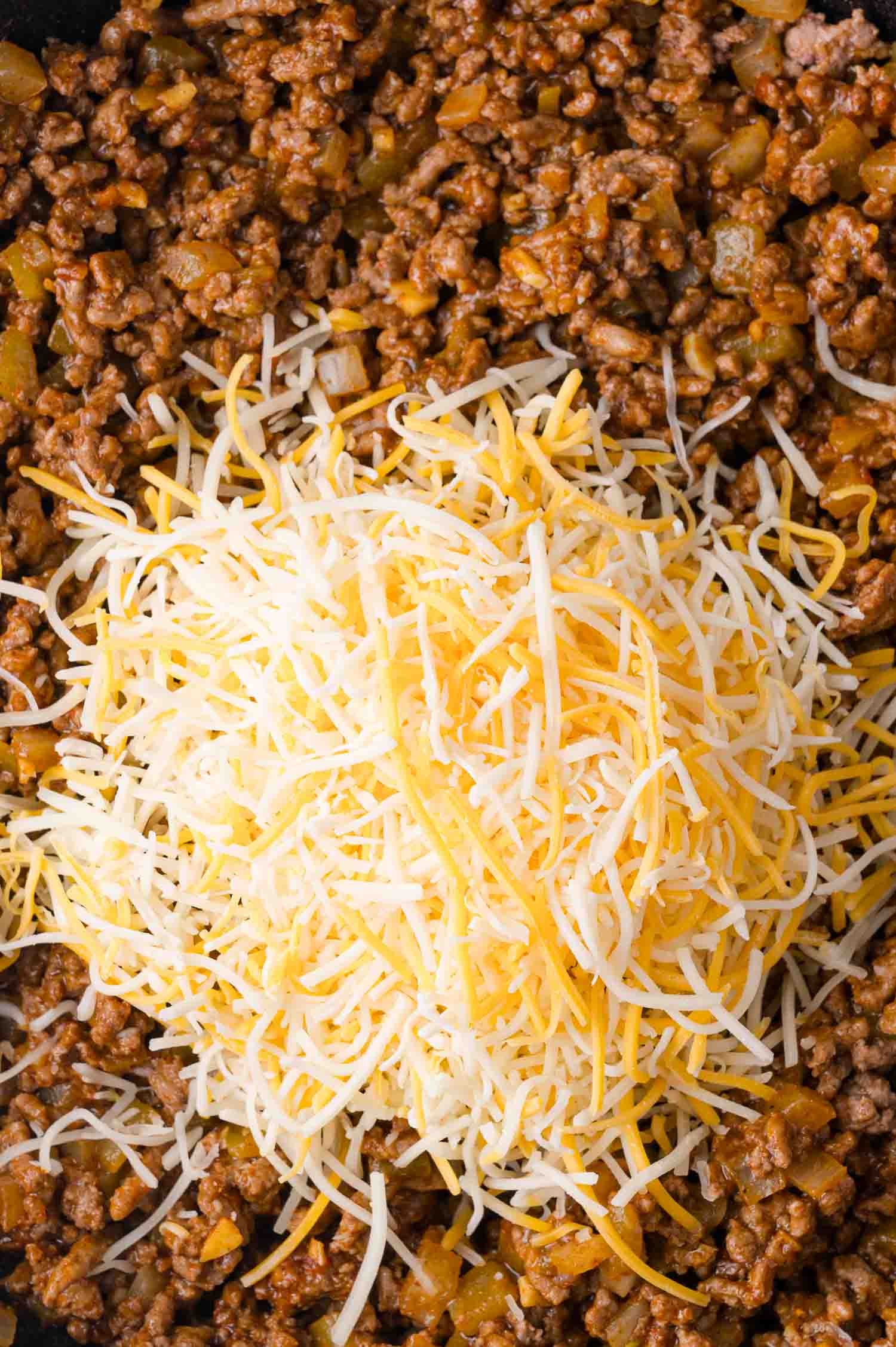 Ground meat mixture with chopped vegetables, topped with a blend of shredded cheddar and mozzarella cheese.