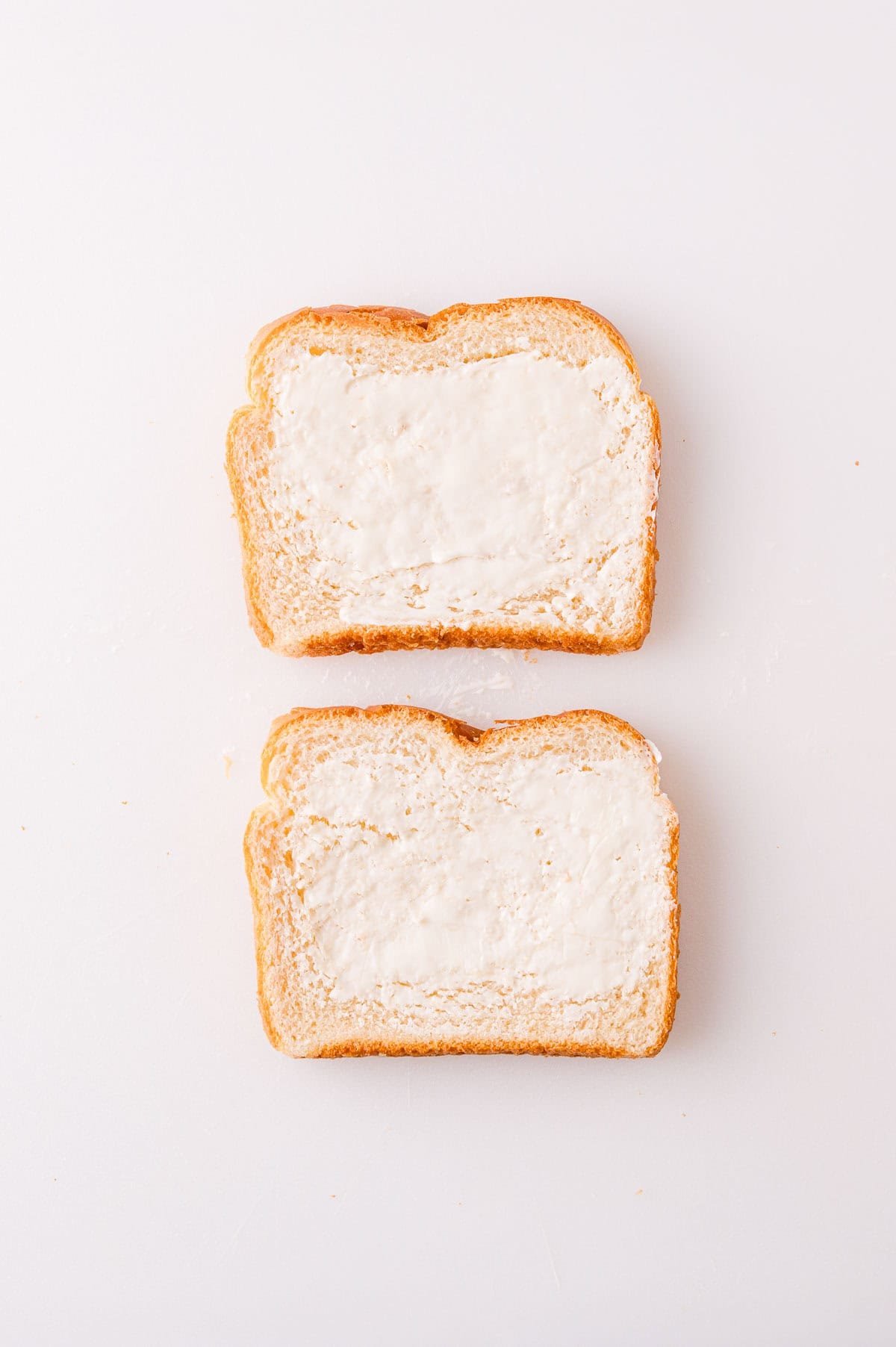 Two slices of bread with butter spread on top, placed on a white surface.