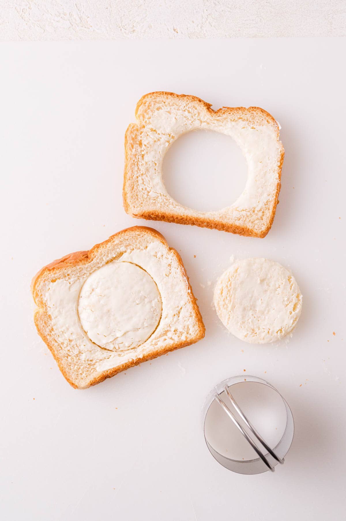 Two slices of bread with butter, one with a circular cutout, the other with a matching circular piece. A round cutter is nearby.