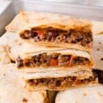 Three stacked quesadilla slices filled with ground beef, black beans, and diced red peppers, placed on top of more quesadillas.