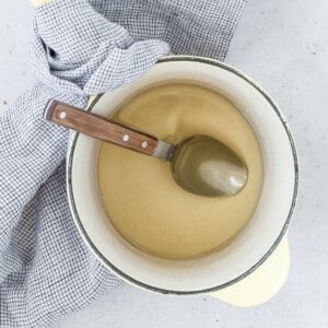 A pot of simple syrup with a wooden-handled spoon on a checkered cloth background.