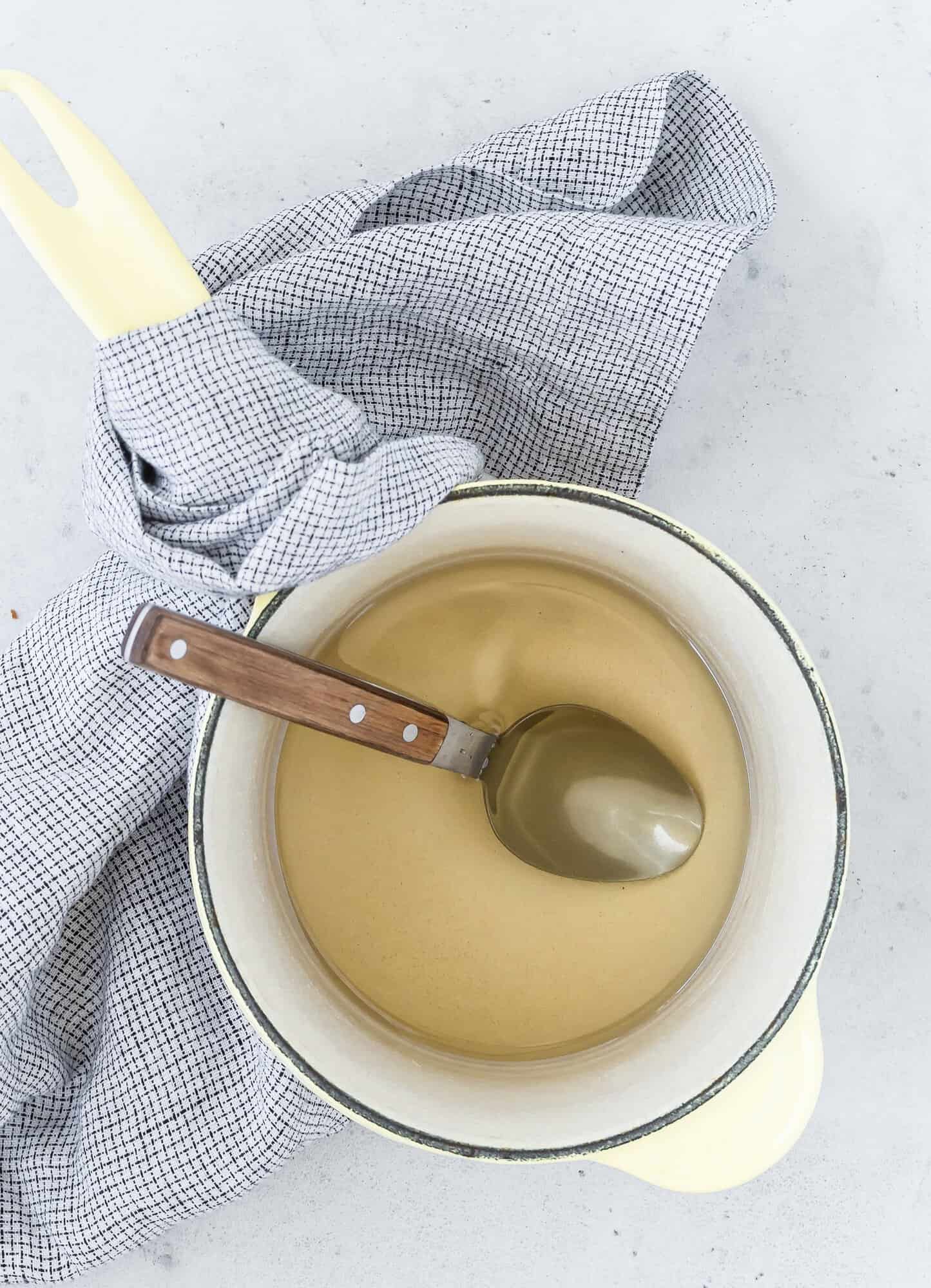 A pot of simple syrup, placed on a checked cloth on a light gray surface.