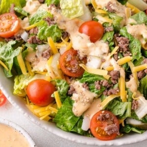 Salad with lettuce, cherry tomatoes, ground beef, shredded cheese, onions, and sesame seed topping in a white bowl.