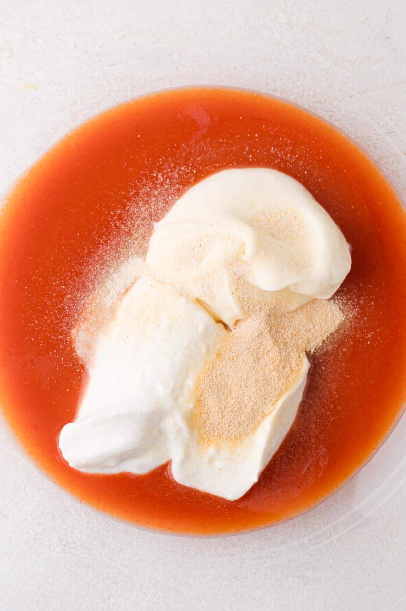A bowl containing tomato sauce, mayonnaise, yogurt, and seasoning powder on a light surface.