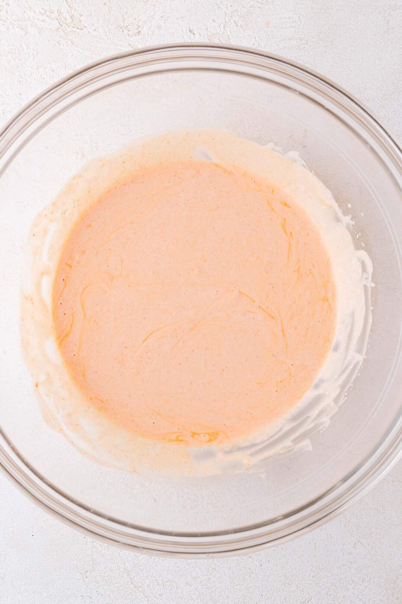A clear glass bowl containing a creamy, light orange mixture sits on a white surface.