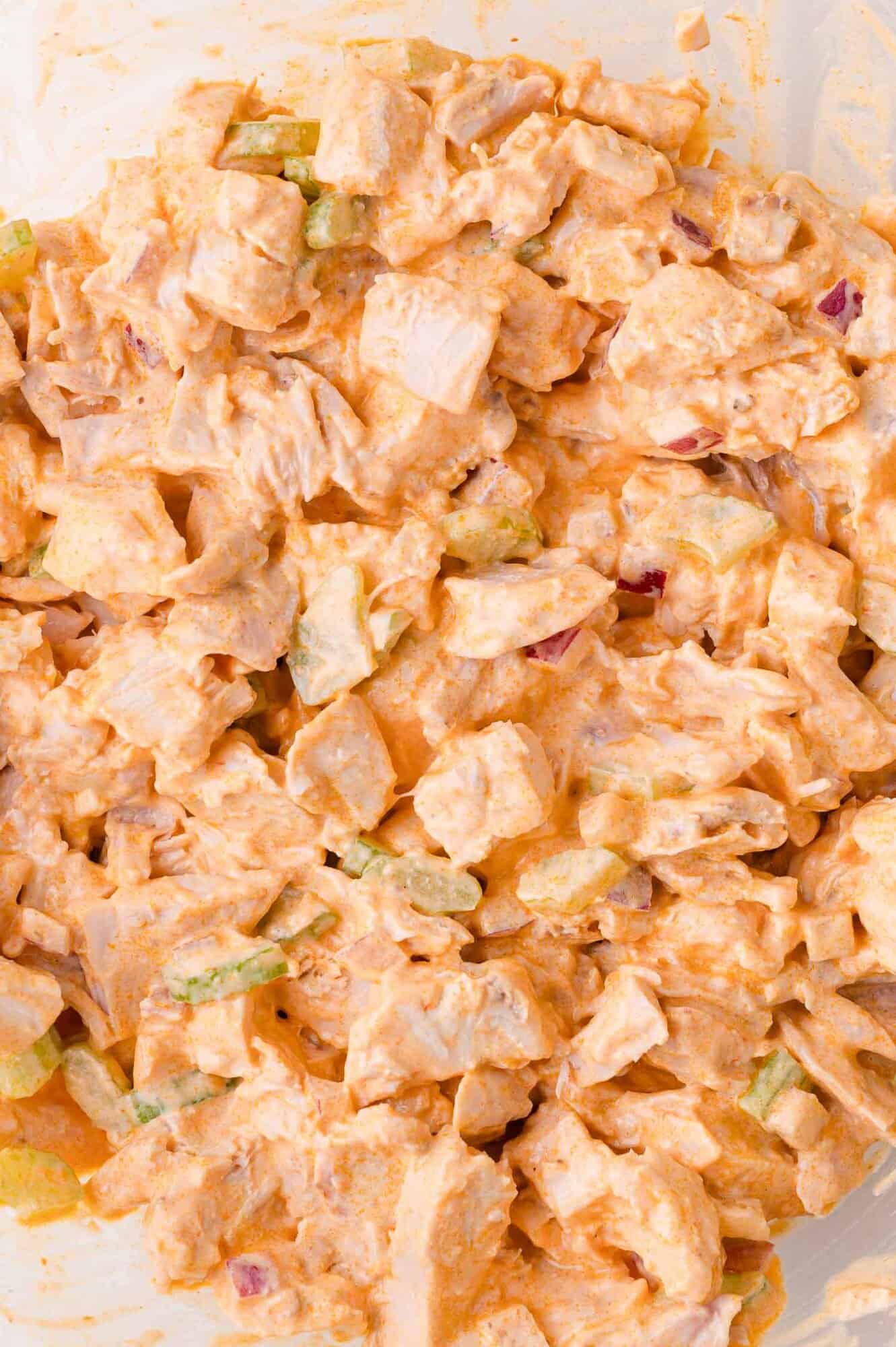 Close-up of a mixed chicken salad with diced chicken, celery, and red onion coated in a creamy, orange-colored dressing.