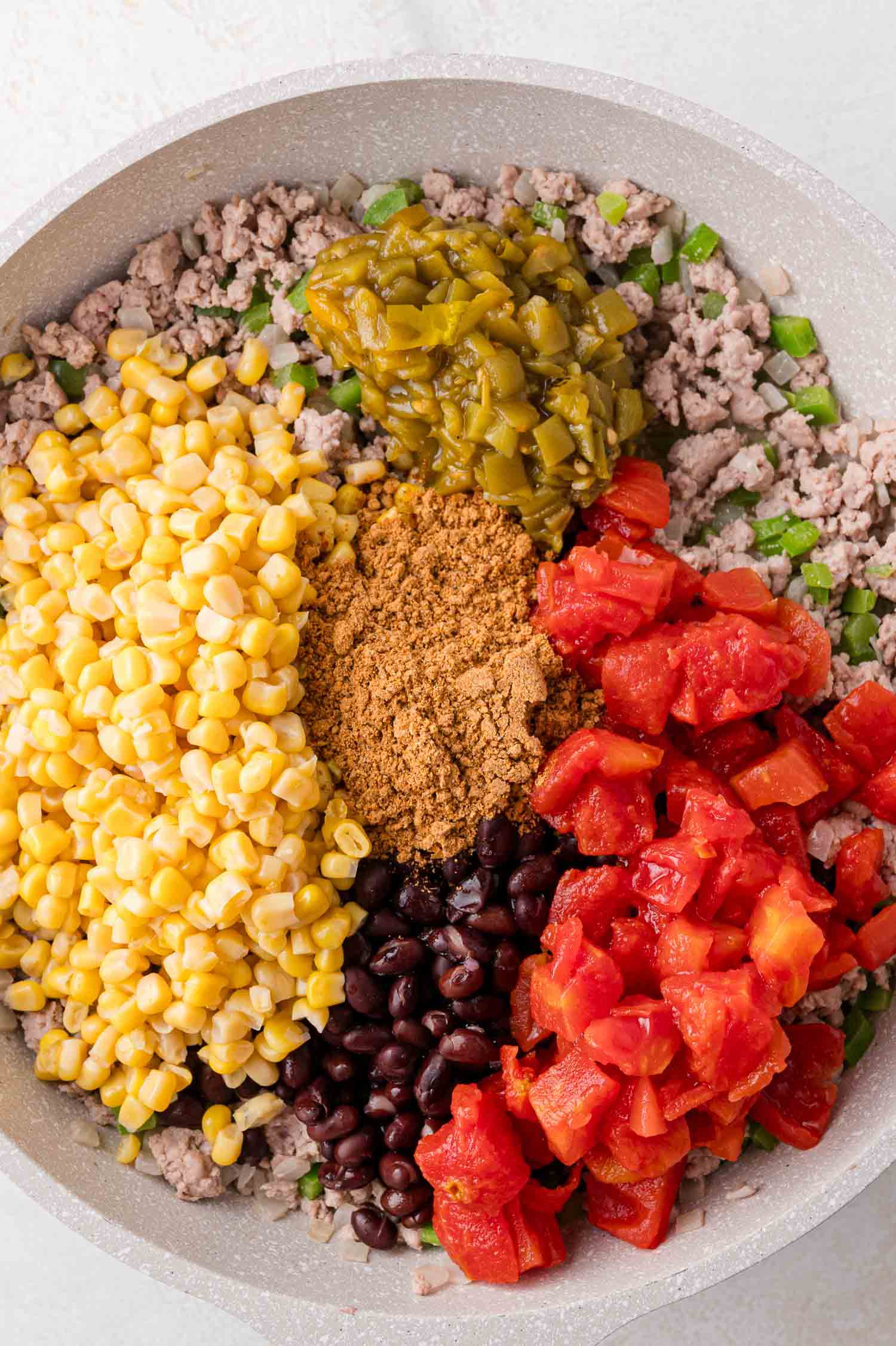 A skillet filled with ground meat, corn, black beans, diced tomatoes, green chilies, and taco seasoning, all arranged in separate sections.