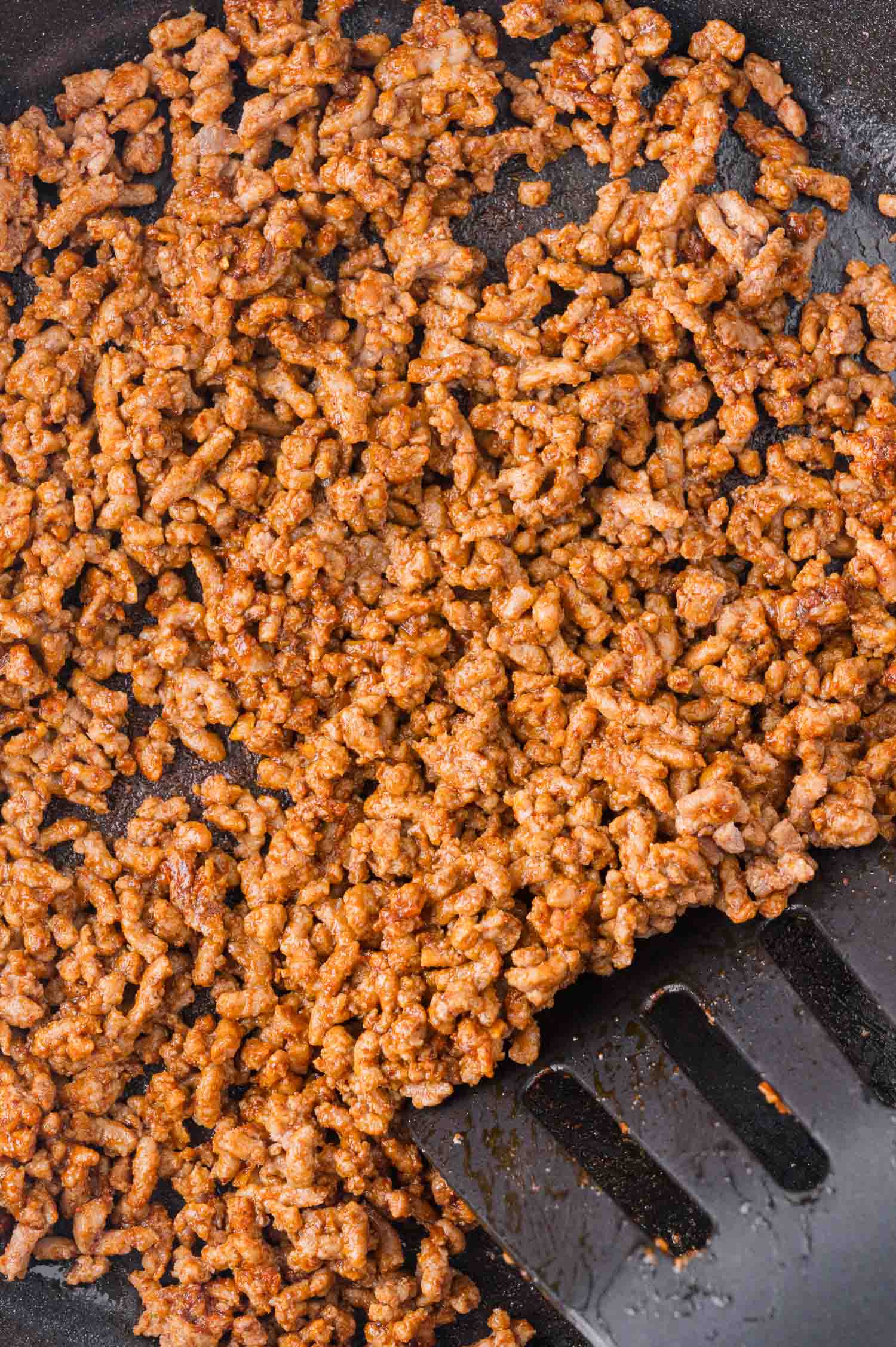 Ground beef cooking in a skillet, browned and evenly spreading with a spatula.