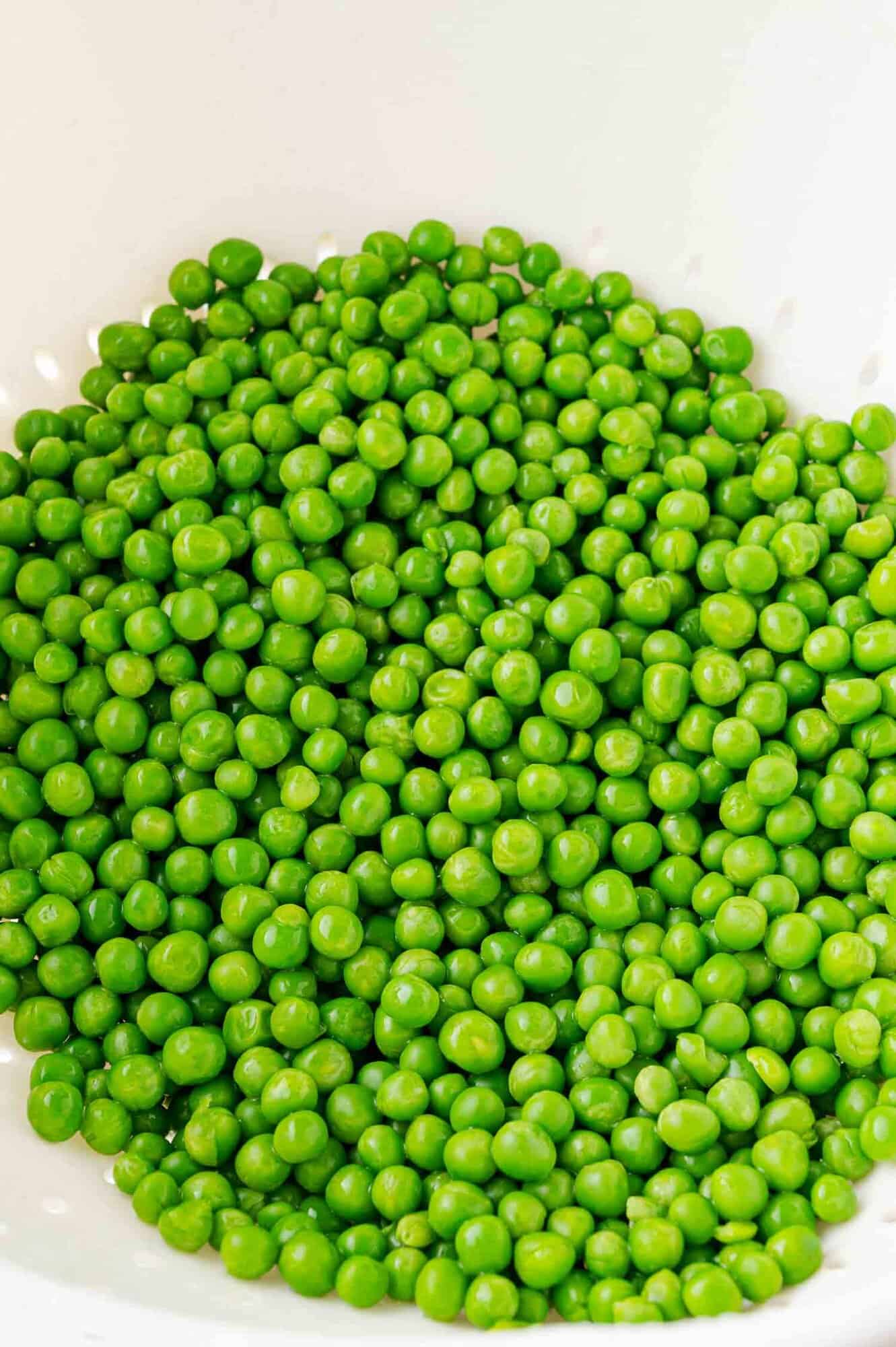 A pile of bright green peas fills a white bowl.