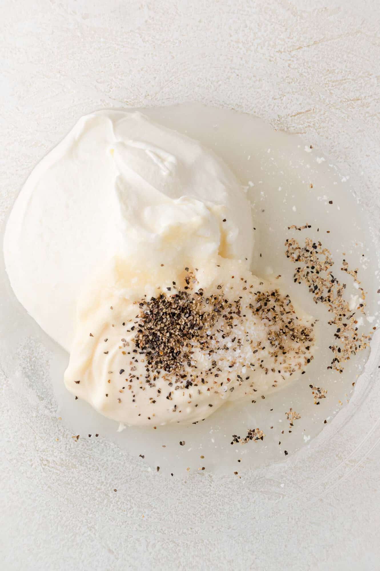 A bowl containing mayonnaise, sour cream, vinegar, salt, and ground black pepper.