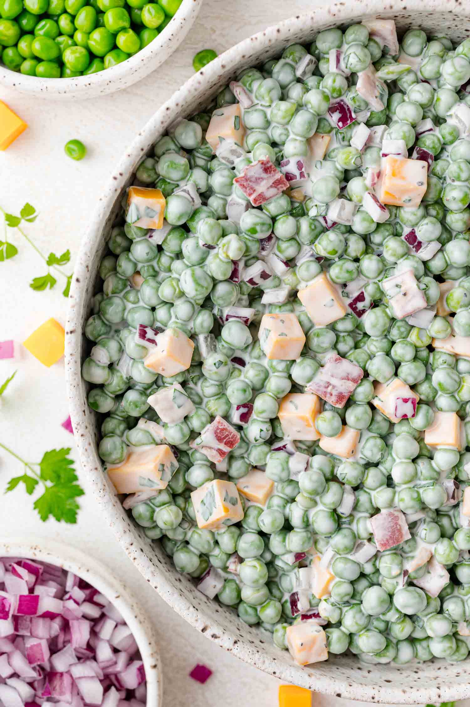 A bowl of pea salad with green peas, diced cheddar cheese, chopped red onions, and a creamy dressing, viewed from above.