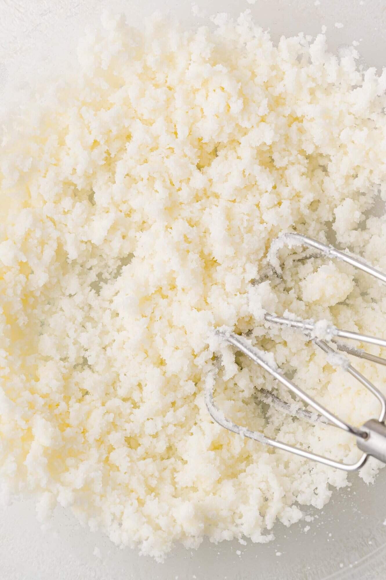 Electric mixer beaters mixing creamed butter and sugar in a bowl, forming a light, fluffy texture.
