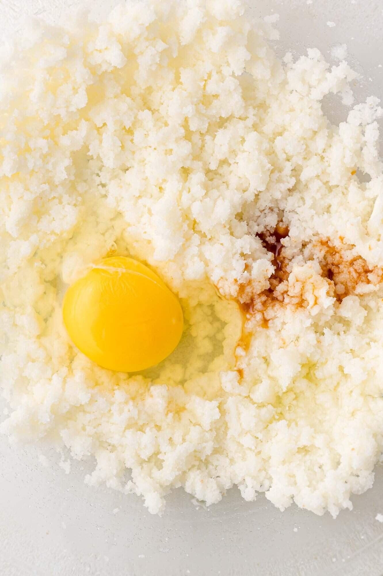 An egg, vanilla extract, and creamed butter with sugar are combined in a mixing bowl.