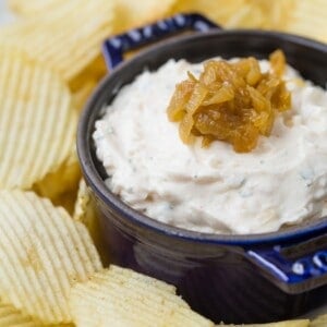 A dark blue bowl with creamy onion dip topped with caramelized onions, surrounded by ripple-cut potato chips.