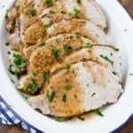 Slices of roasted pork loin garnished with chopped parsley on a white oval platter.