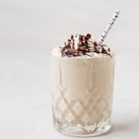 A glass of whiskey milkshake topped with whipped cream and chocolate syrup, served with a striped straw.