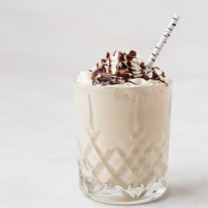 A glass of whiskey milkshake topped with whipped cream and chocolate syrup, served with a striped straw.