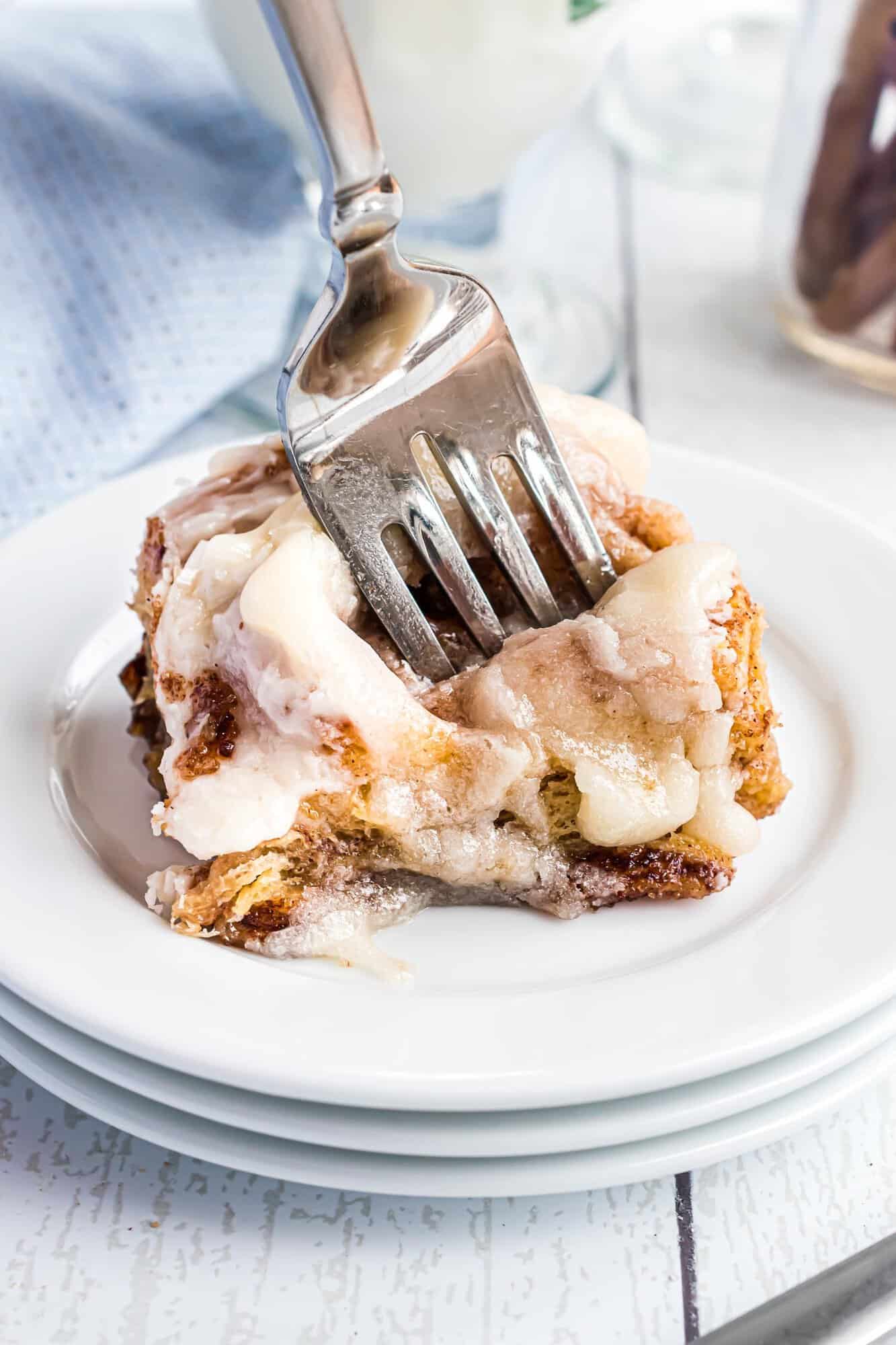 A fork cutting into a frosted cinnamon roll on a stack of white plates.