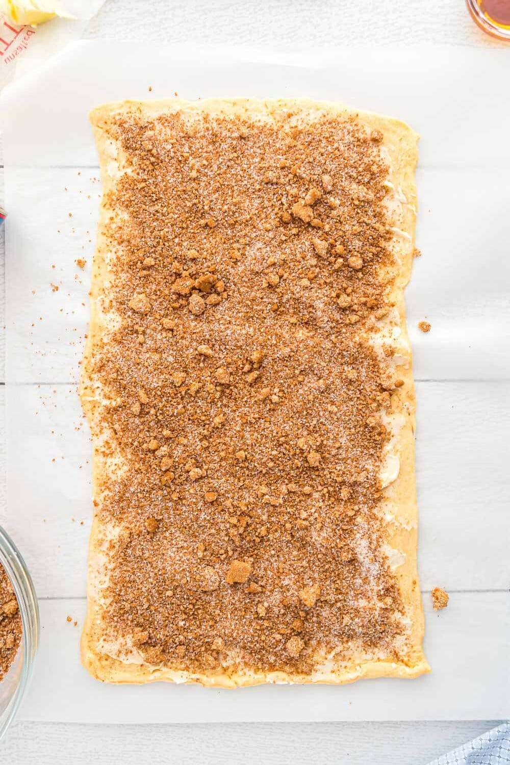 A rectangular sheet of dough covered with an even layer of cinnamon sugar mixture on a sheet of parchment paper.