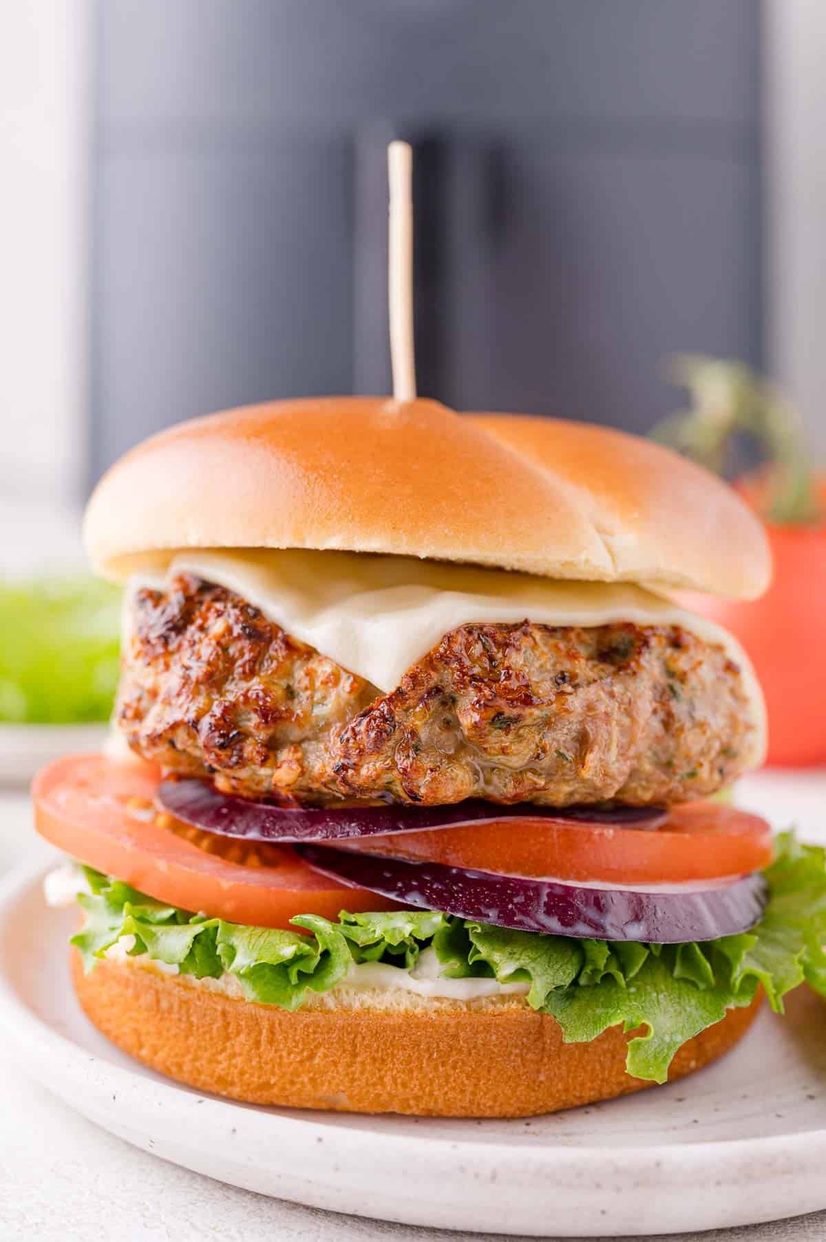 A air fried turkey burger with lettuce, tomato, red onion, and cheese on a bun, served on a white plate.