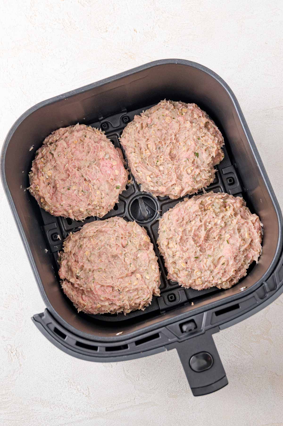 Four raw turkey burger patties are placed inside an air fryer basket, ready to be cooked.