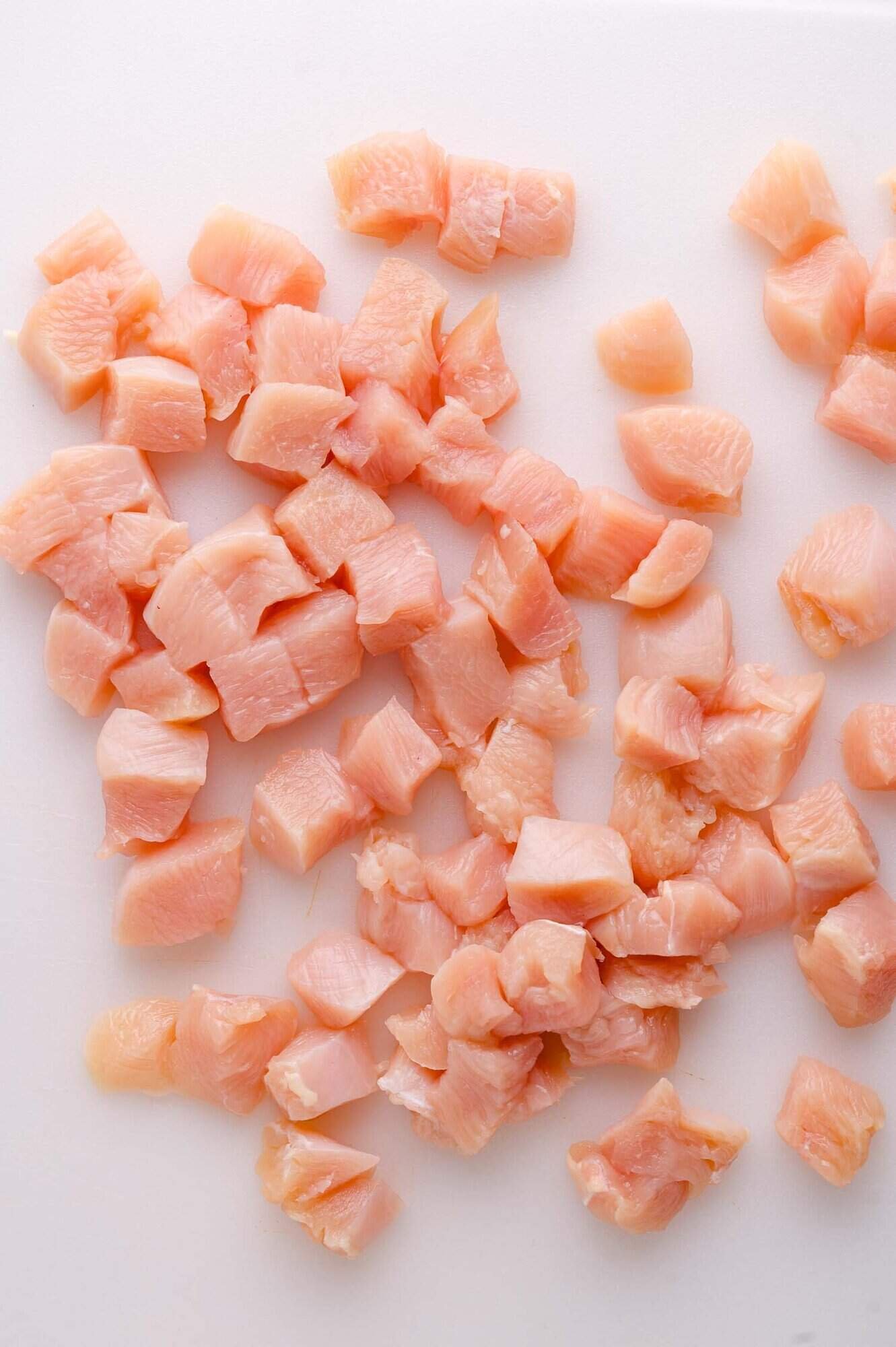 Diced raw chicken pieces spread out on a white cutting board.