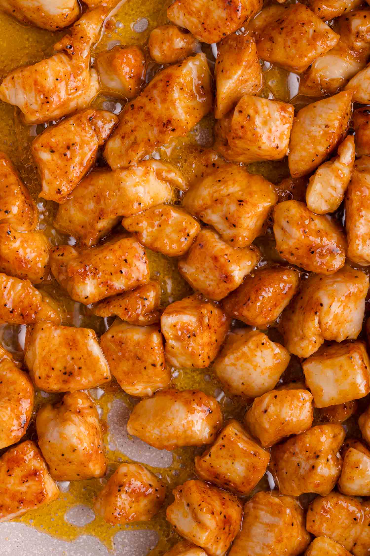 Cooked, seasoned chicken breast pieces coated in a glossy, orange-brown sauce on a white surface.
