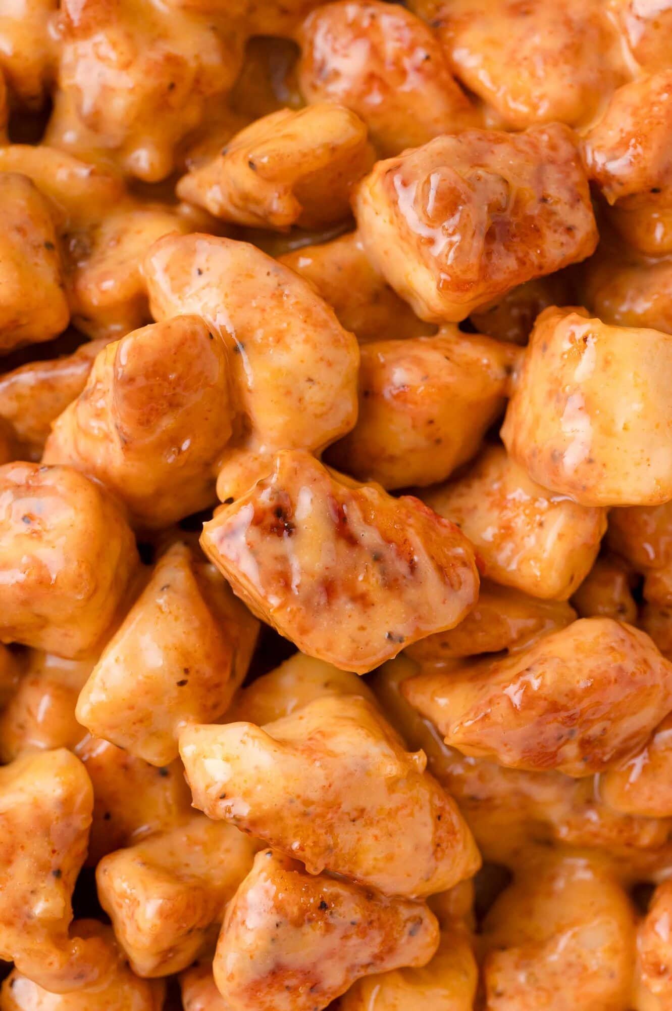 Close-up view of bite-sized chicken pieces coated in a creamy orange sauce.