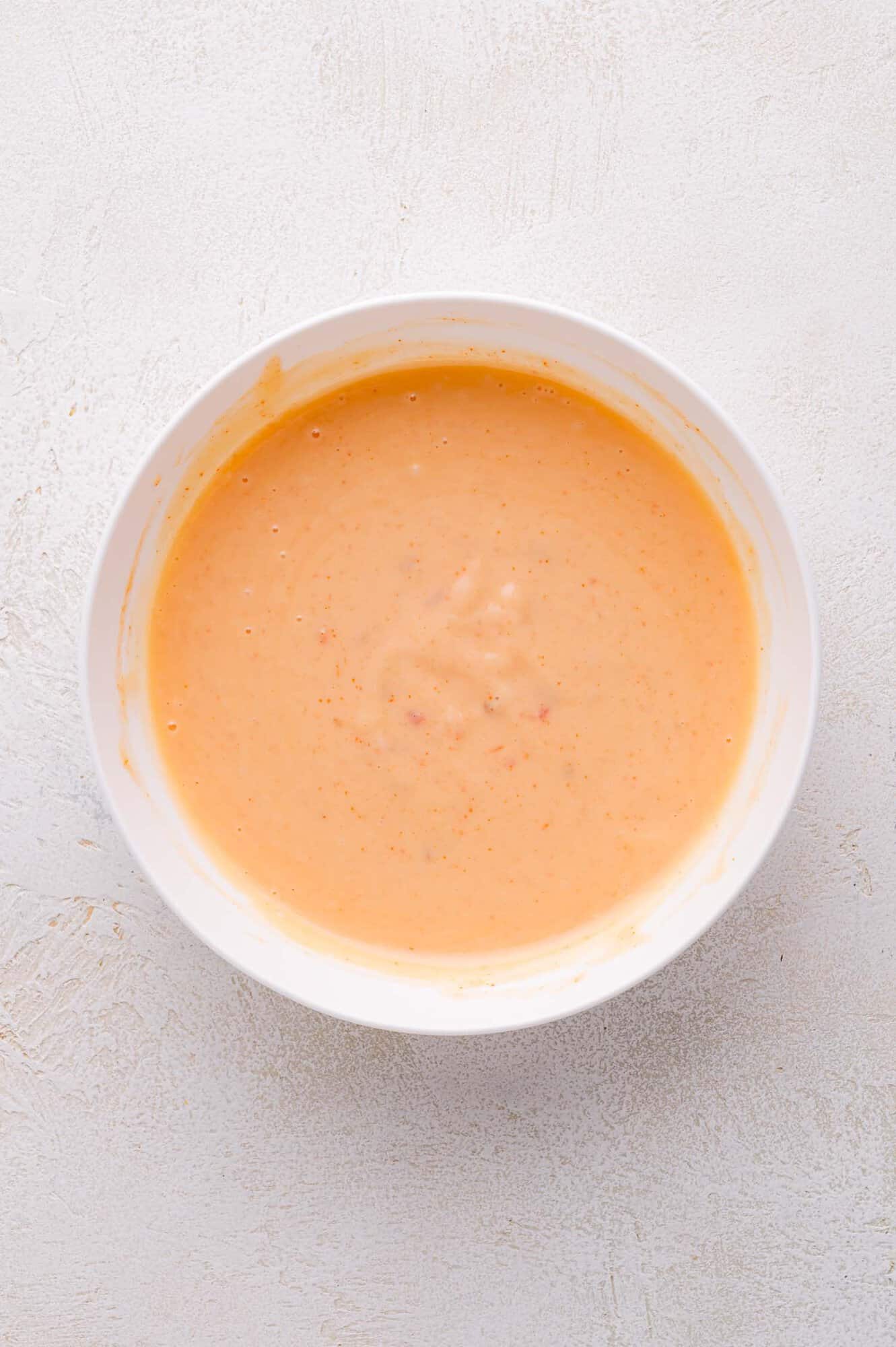A white bowl filled with a creamy, orange-colored sauce sits on a light textured surface.