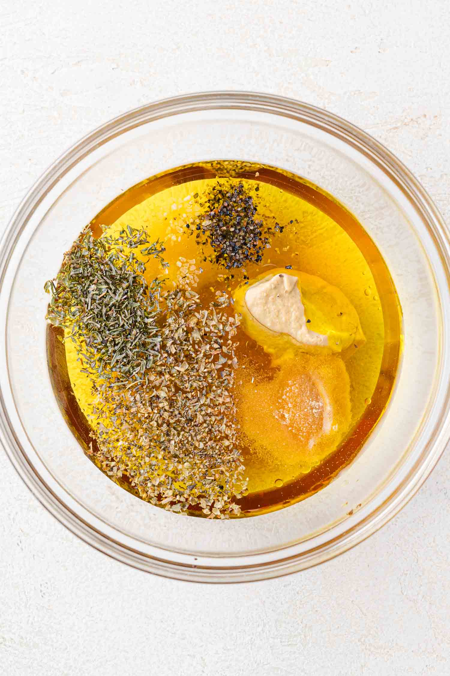A glass bowl containing salad dressing ingredients on a white surface.